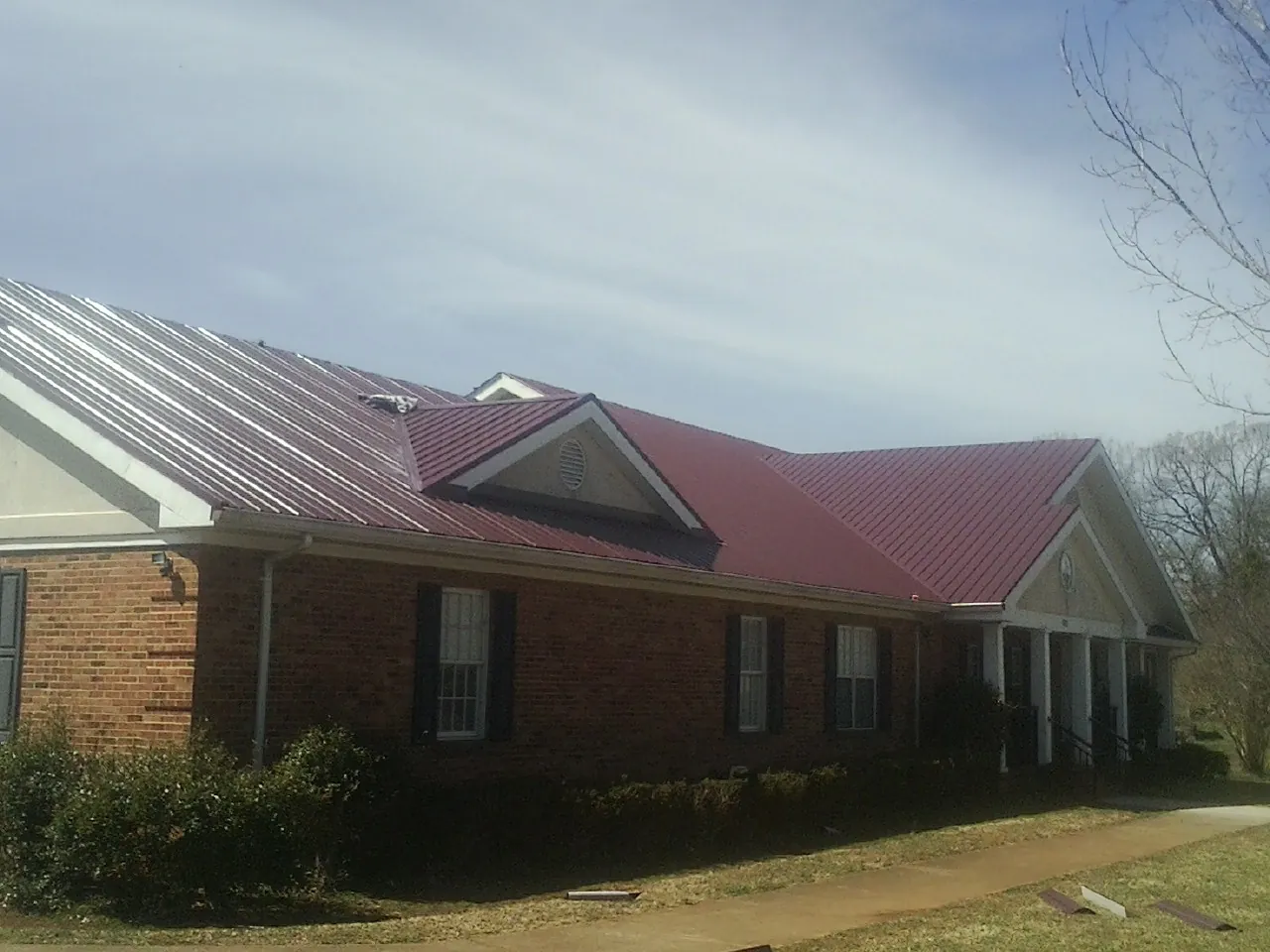 Red metal roof with gabled entries on a long brick building, from a Hail Damage Roof Repair job in Schuylkill Haven