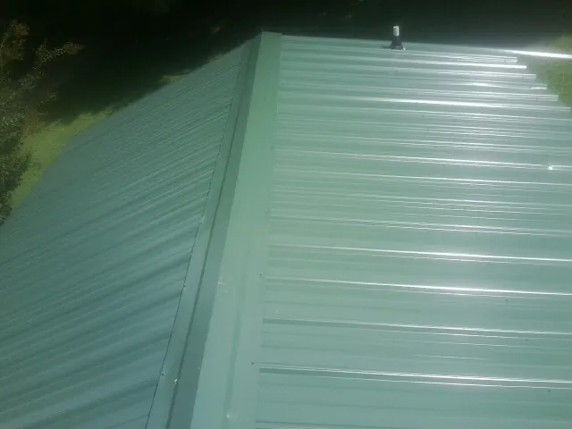 New green metal panels meeting at the ridge of a roof — Flat Roof Repair work by our crew in Schuylkill Haven