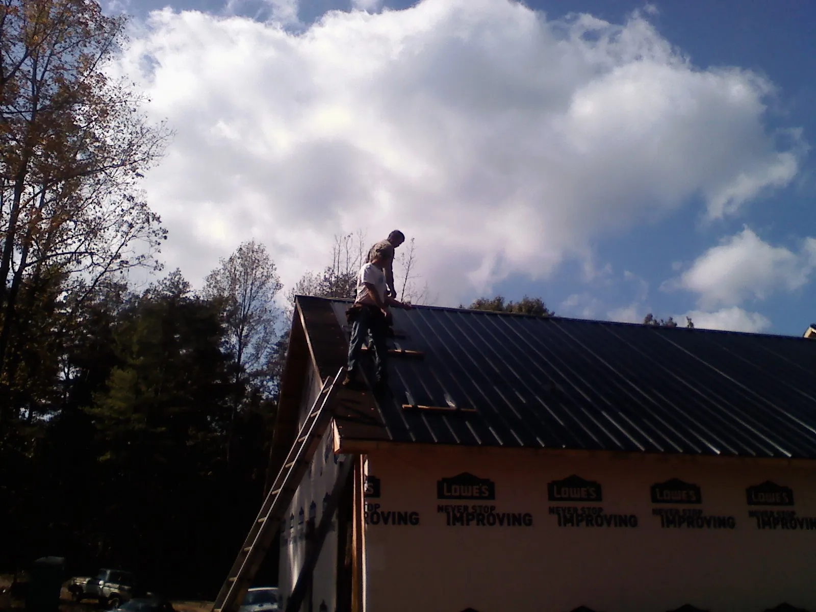 Roofer fastening dark metal panels high against a cloudy sky, from a Roof Inspection job in Schuylkill Haven