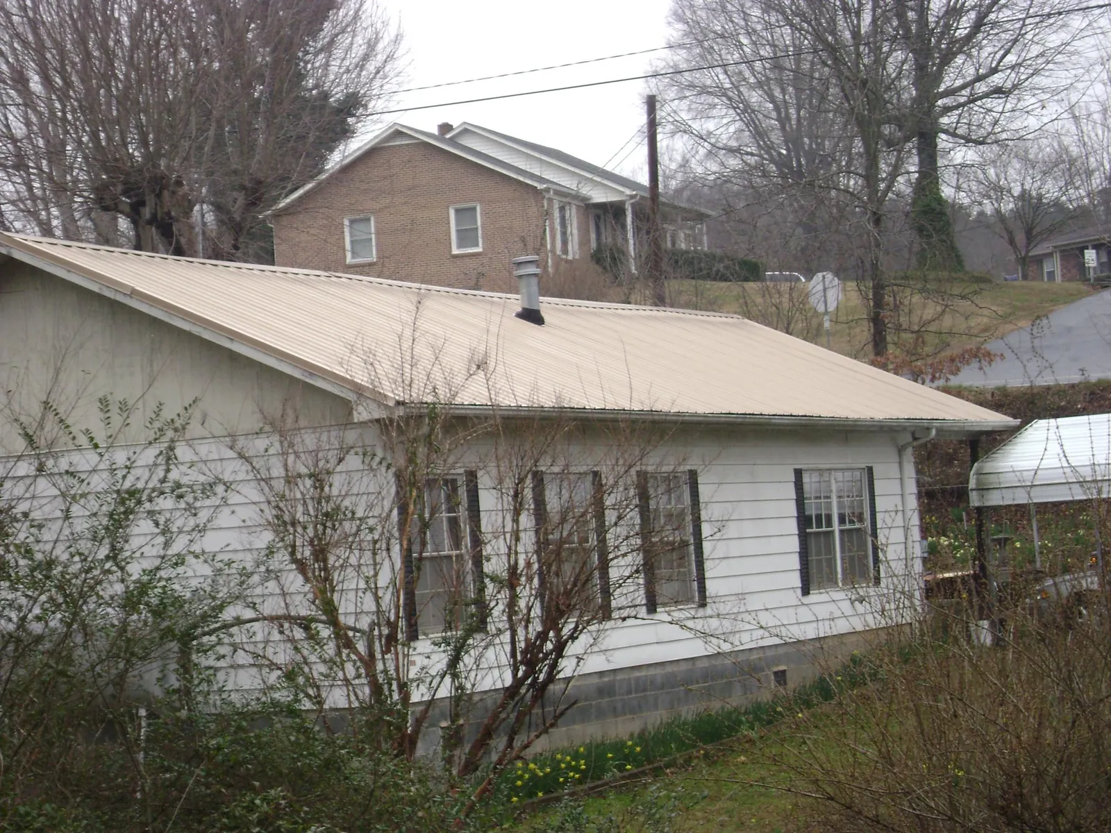 Tan metal roof on a white sided house set into a hillside — Commercial Roofing by Roofing Brothers in Schuylkill Haven